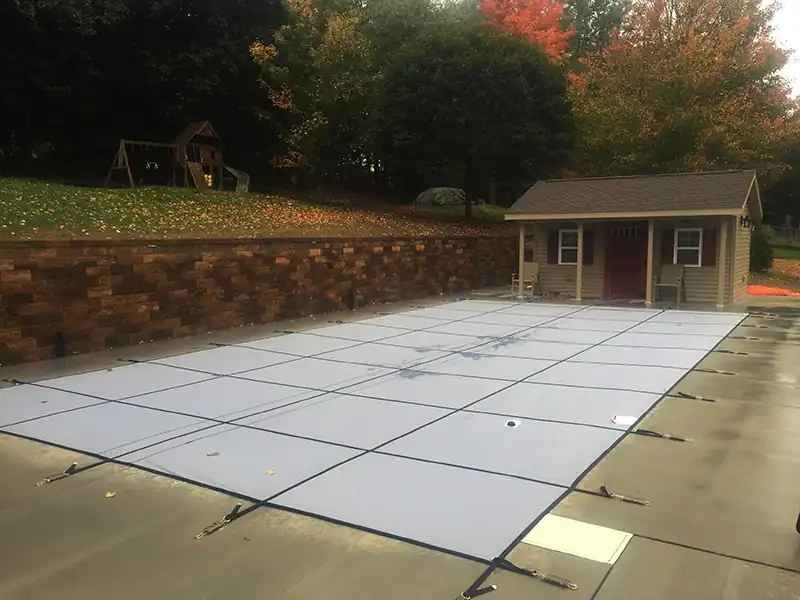 Mesh safety cover over a pool with a brick wall and pool house behind