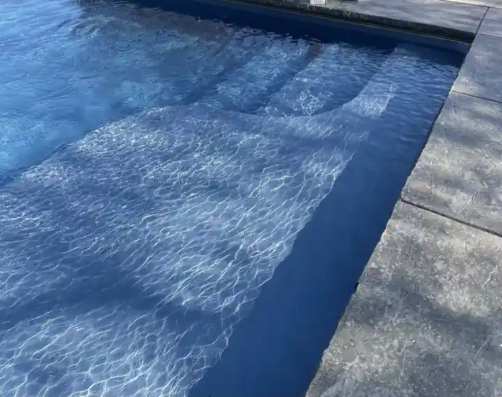 Sunlight caustics rippling across sunken pool steps in clear water