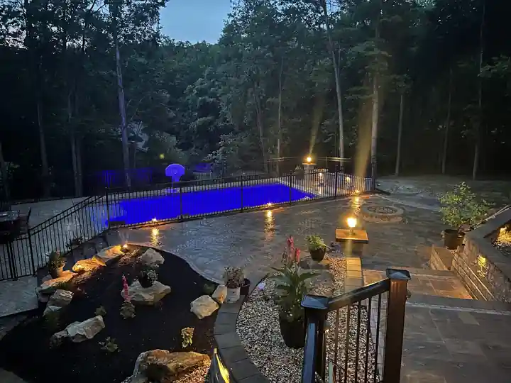 Inground pool lit blue at dusk beside a boulder garden and stone patio