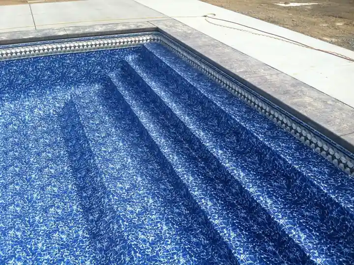 Mosaic pattern vinyl liner across a set of pool steps under clear water