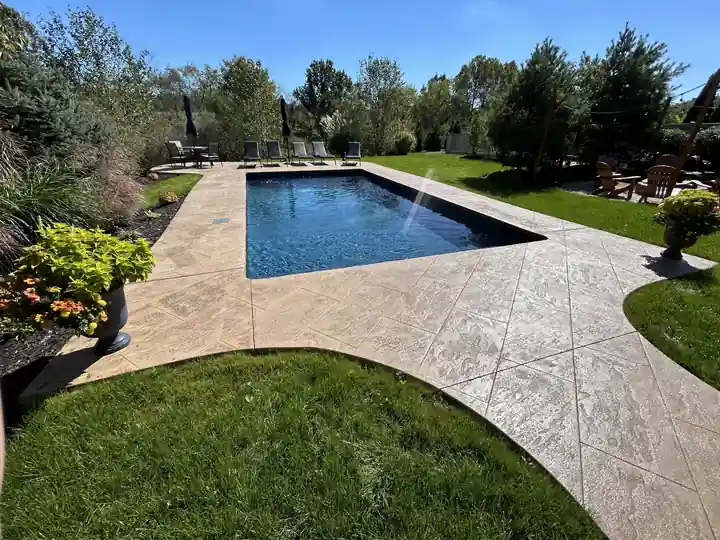 Long rectangular liner pool beside garden beds and a stamped concrete path