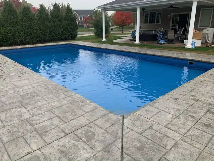 Corner of a stamped concrete pool deck with a covered porch behind
