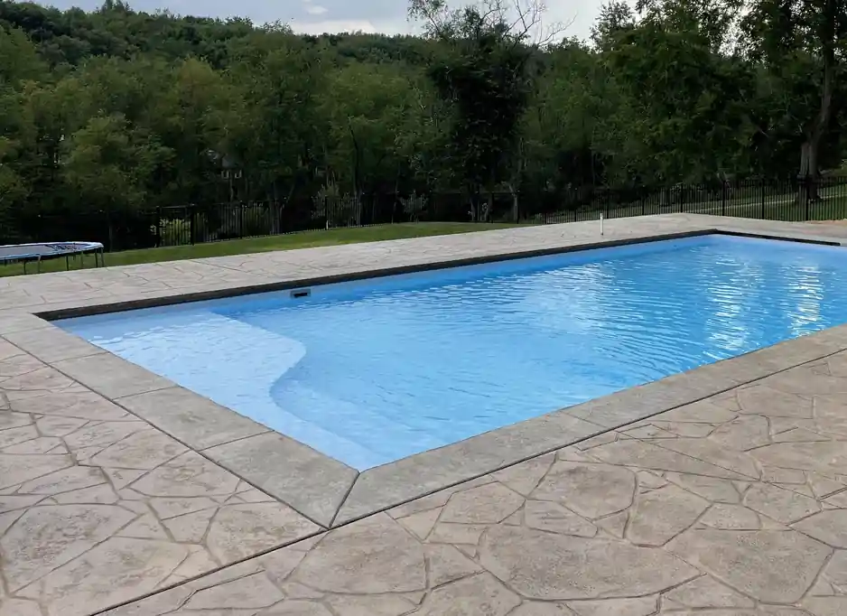 Rectangular liner pool on a stamped deck with a wooded ridge behind