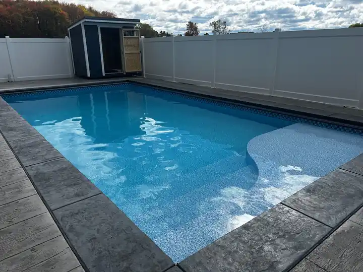 Pool with stamped coping inside a white vinyl fence, a shed in the corner